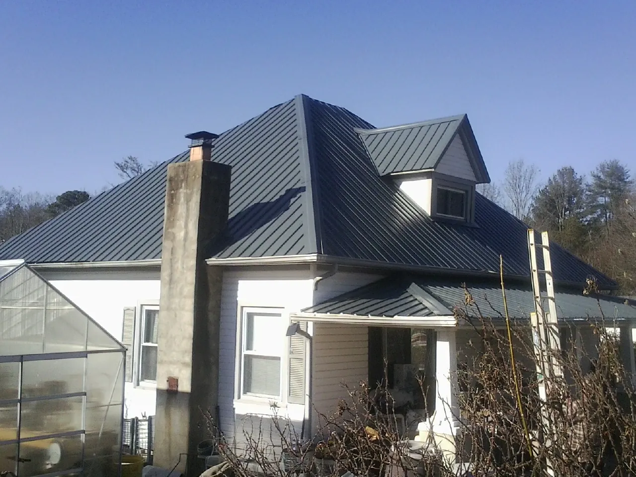 Dark blue standing seam metal roof on a white farmhouse with dormer — Slate & Tile Roof Repair by Roofing Brothers in Poplar Branch