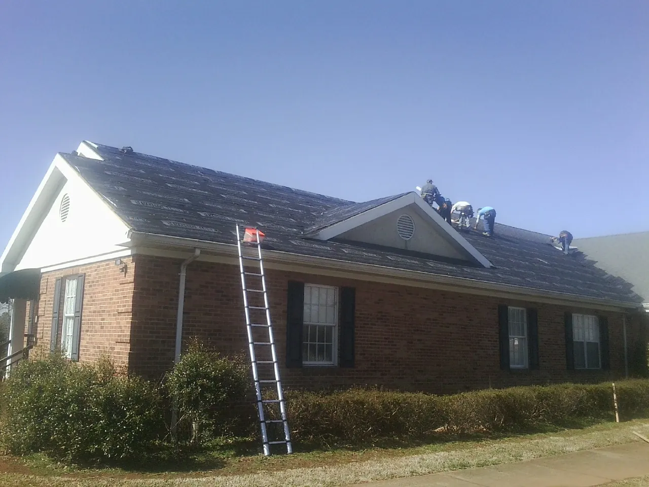 Crew tearing shingles off a brick ranch roof with a ladder set — Emergency Roof Repair work by our crew in Poplar Branch