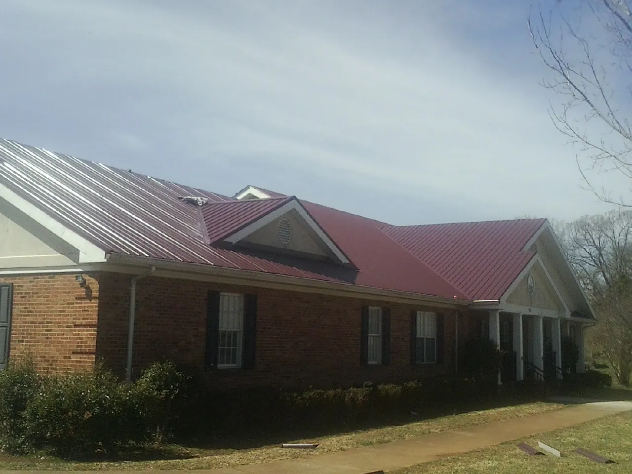 Red metal roof with gabled entries on a long brick building, from a Hail Damage Roof Repair job in Poplar Branch