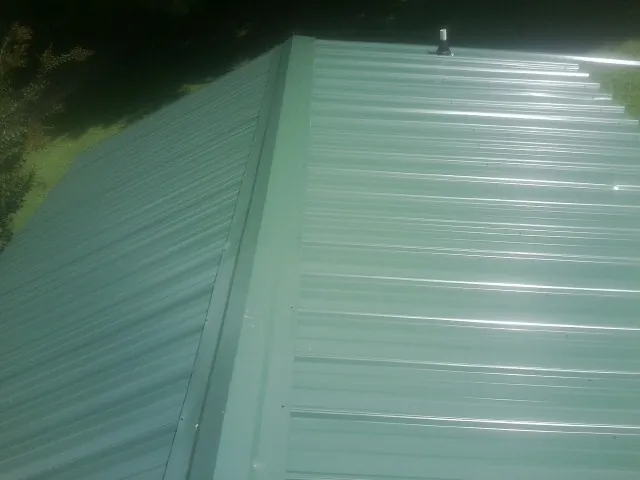 New green metal panels meeting at the ridge of a roof — Flat Roof Repair work by our crew in Poplar Branch