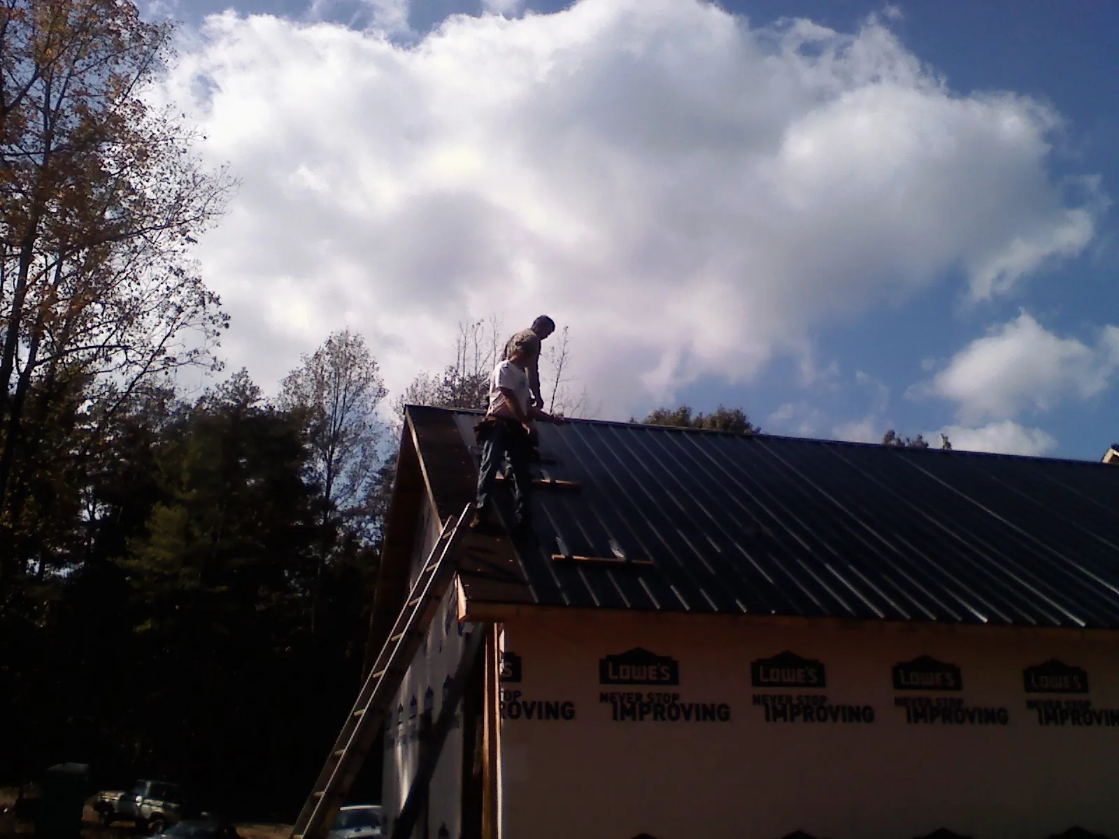 Roofer fastening dark metal panels high against a cloudy sky, from a Roof Inspection job in Poplar Branch