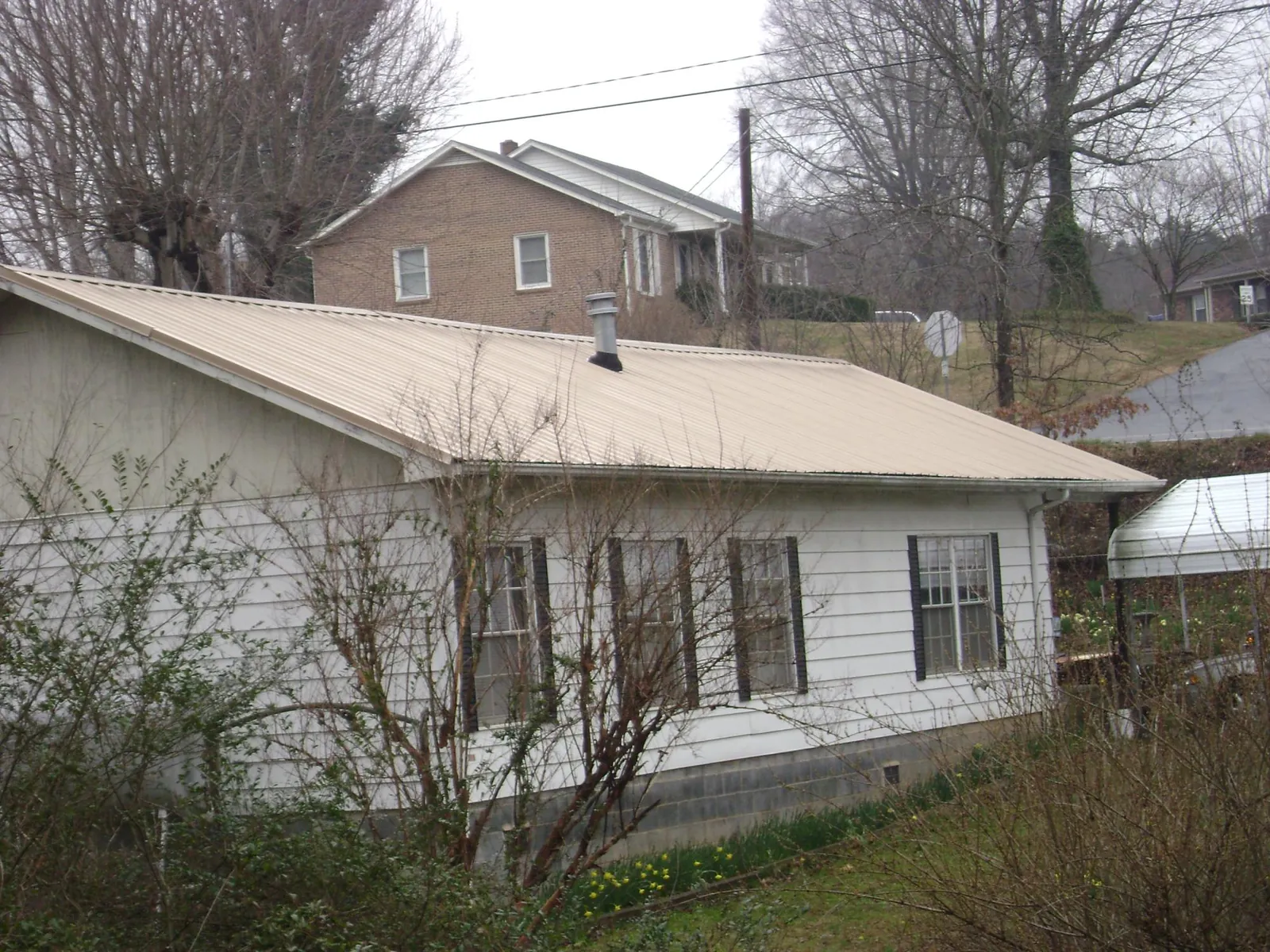 Tan metal roof on a white sided house set into a hillside — Commercial Roofing by Roofing Brothers in Poplar Branch