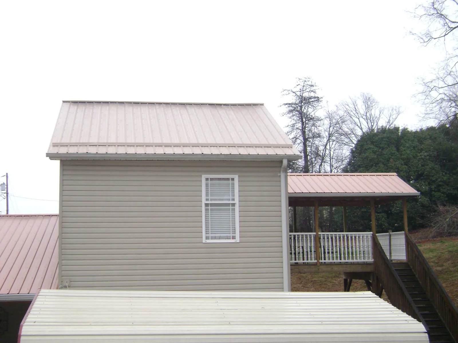Tan metal roofs on a two story addition and attached porch, from a Roof Replacement job in Poplar Branch